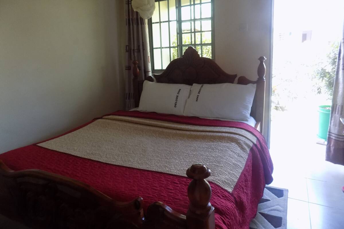 Uma cama com cabeceira, janela com grades e cortina.