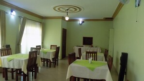 A dining area with multiple tables and chairs, a ceiling fan, and a television mounted on the wall. - Deluxe Hotel - Ishaka (Ishaka)