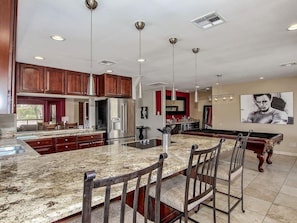 Enjoy cooking in this well-equipped kitchen with a large island, stainless steel appliances, and a pool table nearby.