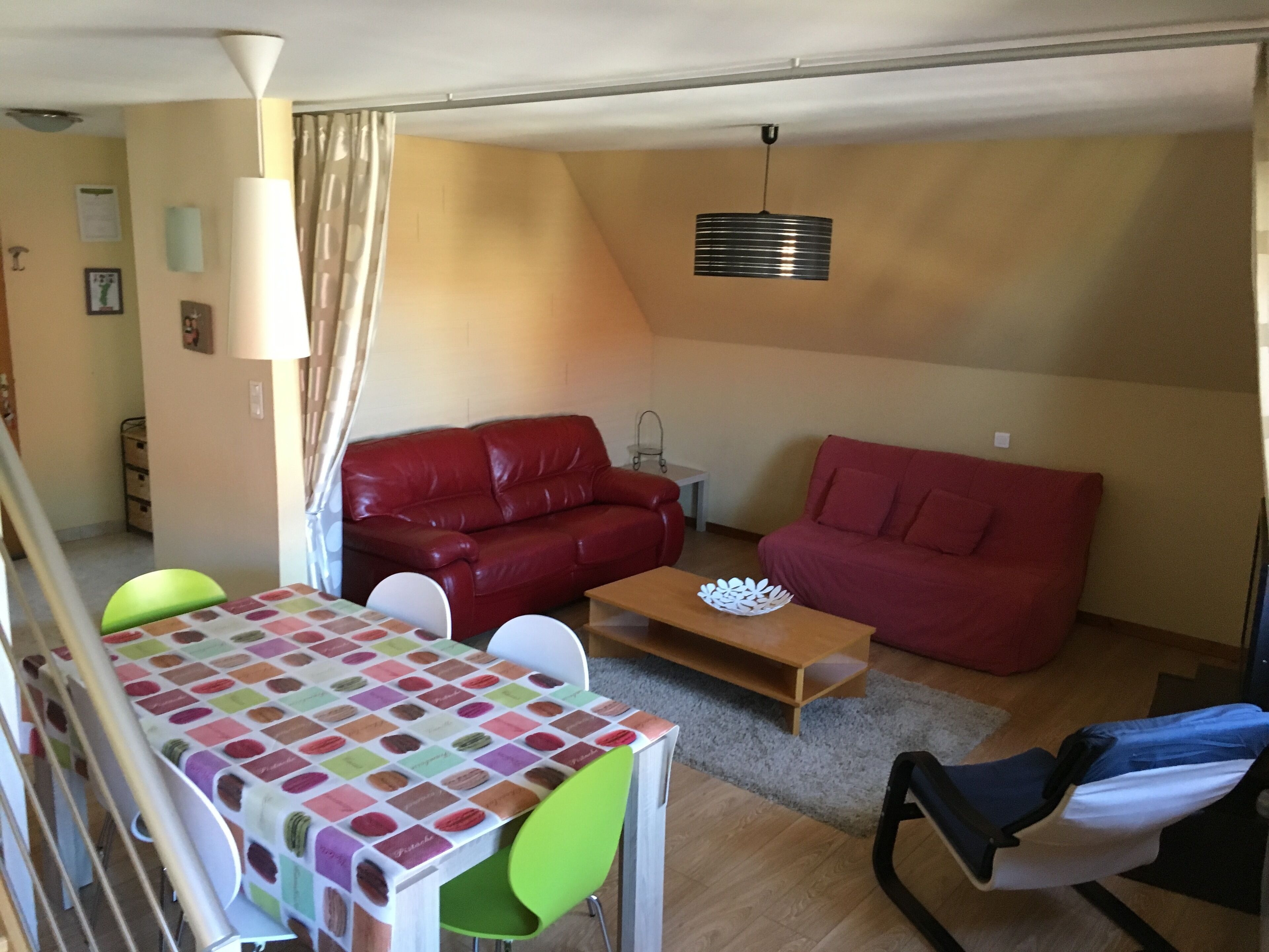 A compact living space with a red sofa, a green chair, a wooden table, and a small white table.