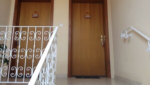 A wooden door with a nameplate, a white metal railing, and a wall-mounted light fixture.