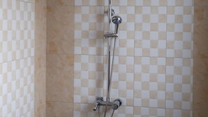 Une salle de bain avec un mur recouvert de carreaux à motifs, une douche équipée d’un pommeau de douche à main et un robinet fixé au mur.