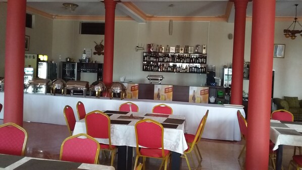 Un restaurant avec un long comptoir, des chaises rouges et un mur recouvert d’étagères à bouteilles.