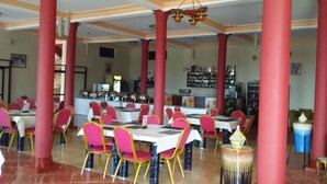 Un restaurant avec des piliers rouges, des chaises roses et des tables blanches.
