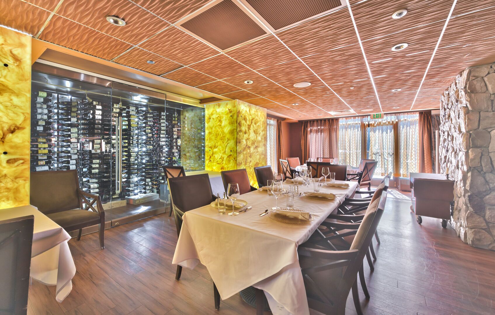 A restaurant with a long table set for dining, wooden ceiling, and a wall of wine bottles.