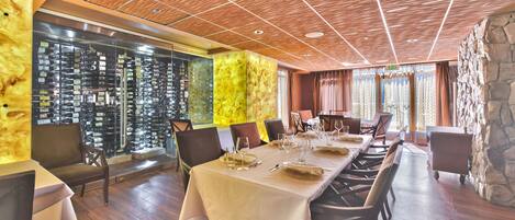 A restaurant with a long table set for dining, wooden ceiling, and a wall of wine bottles.