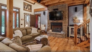 A cozy living room with a stone fireplace, wooden beams, and a television mounted above it.