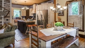 A rustic kitchen with wooden cabinets, a central island, and a dining table with a lace tablecloth.