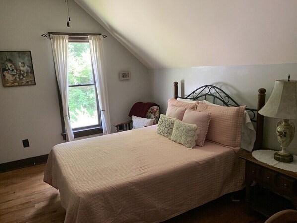 Un dormitorio con una cama, una mesita de noche, una lámpara, una ventana con cortinas y un cuadro en la pared.