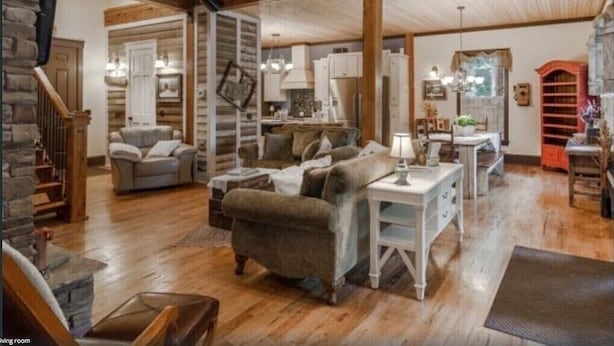 A spacious living room with a wooden ceiling, a staircase, and a dining area with a table and chairs.