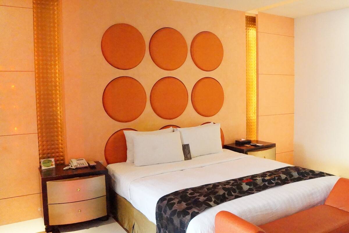 Habitación de hotel con cama, mesita de noche, silla y pared con diseños circulares.