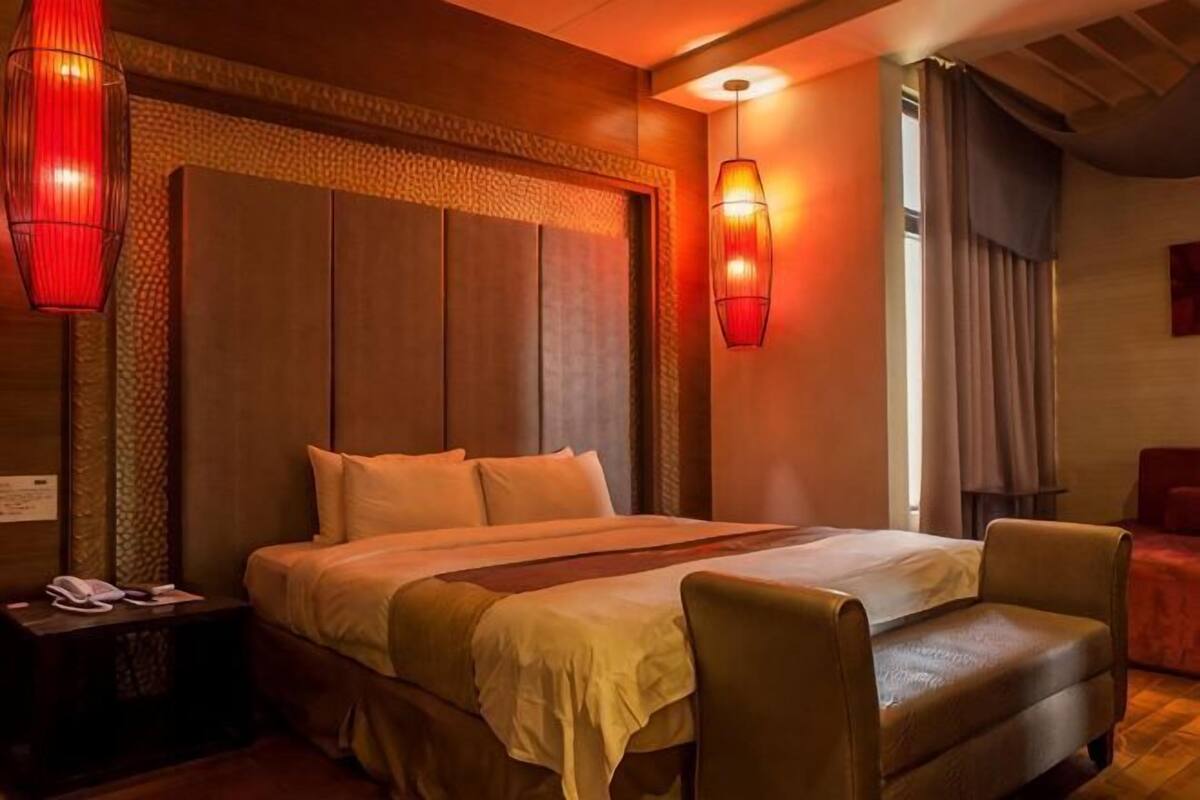 Habitación de hotel con una cama grande, una mesita de noche, una silla y una ventana con cortinas.