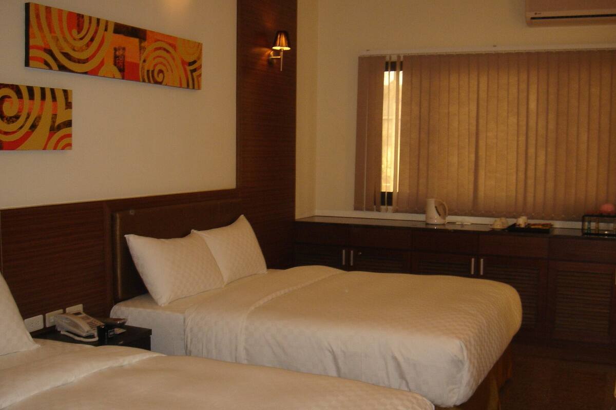 Una habitación de hotel con dos camas, un escritorio pequeño con teléfono y una ventana con cortinas.