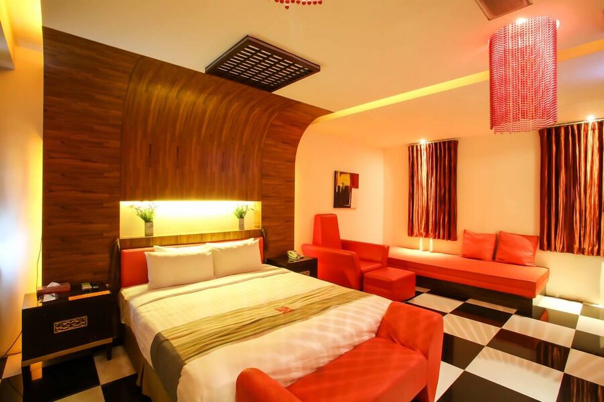 Una habitación de hotel moderna con una cama grande, una zona de estar con sillones rojos y un suelo a cuadros.