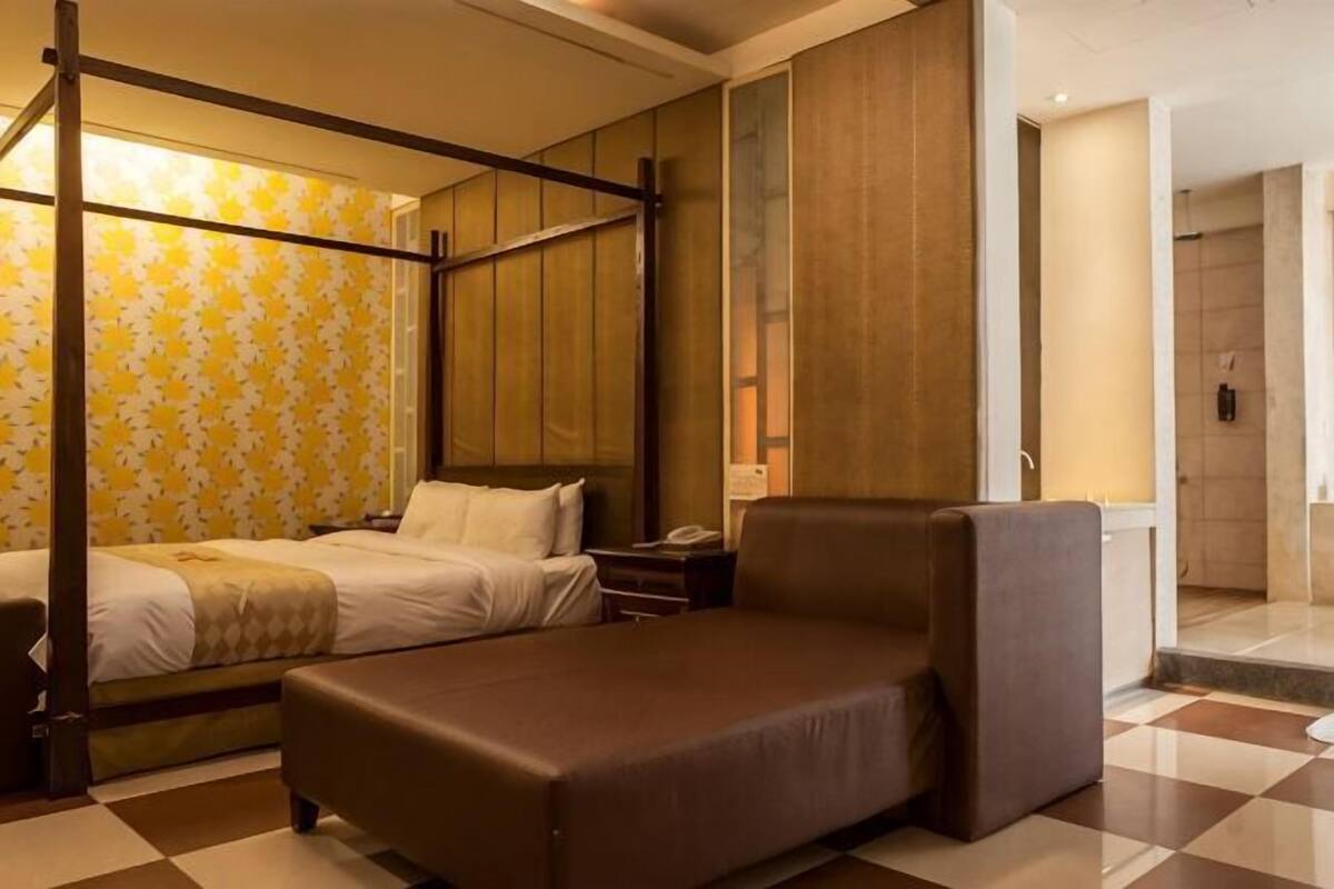 Una habitación de hotel con cama con dosel, sofá cama, una mesita de noche y una mesilla.