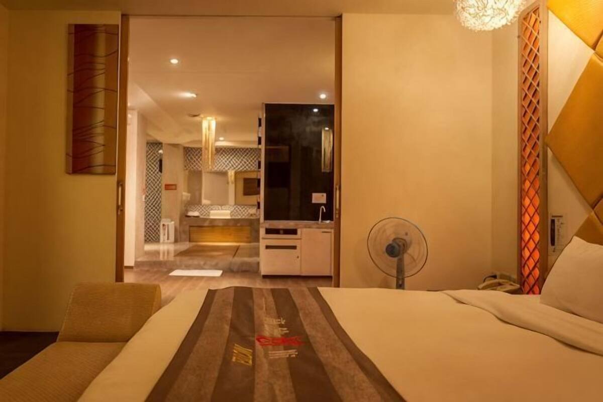 Una habitación de hotel con cama, escritorio, silla, ventilador y vistas a la cocina y el baño.
