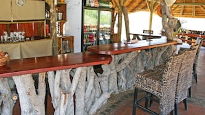 A rustic bar area with a wooden counter, wicker chairs, and a refrigerator stocked with beverages.