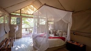 A tent with a bed, a fan, and a table.