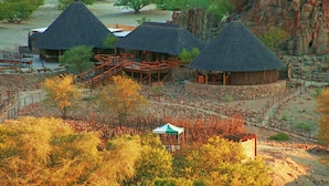 A thatched-roof structure with a wooden deck and a small green tent in the foreground.