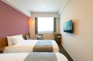 A hotel room with two beds, a television, a small table, and a window with curtains.