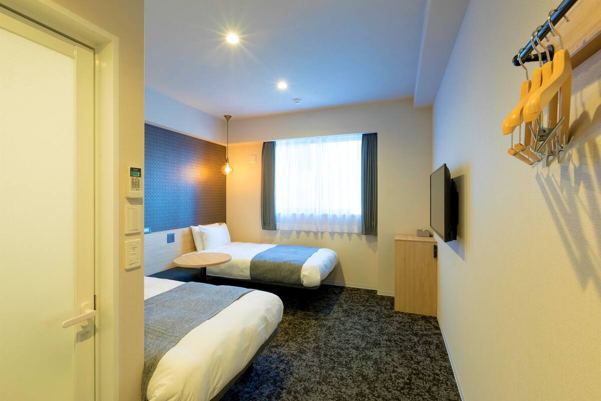 A hotel room with two beds, a TV, a window with curtains, and a wall-mounted towel rack.