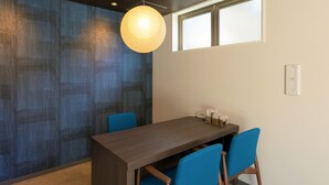 A modern dining area with a dark wooden table, blue chairs, a hanging light fixture, and a window with blinds. - M’s Hotel Kyoto Station Taruya (Kyoto)
