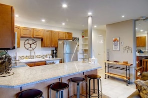 Una cocina con armarios de madera, un refrigerador de acero inoxidable, encimera de granito y una zona de bar con taburetes.
