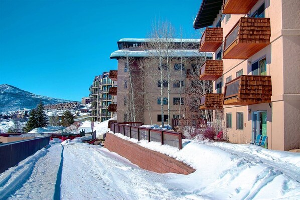 A snow-covered street with multi-story buildings, including balconies and a clear view of the surrounding mountains.