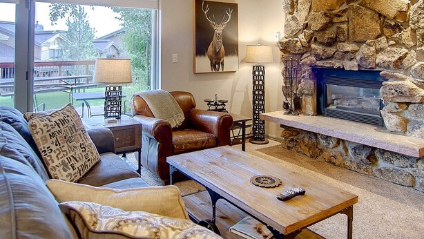 A cozy living room with a stone fireplace, leather sofa, and a view of the outdoors.