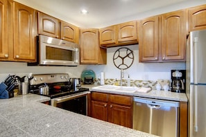 A kitchen with wooden cabinets, stainless steel appliances, granite countertops, and a decorative wall piece. - Ski In & Walk Out-Patio with Slope Views-HotTub (Steamboat Springs)