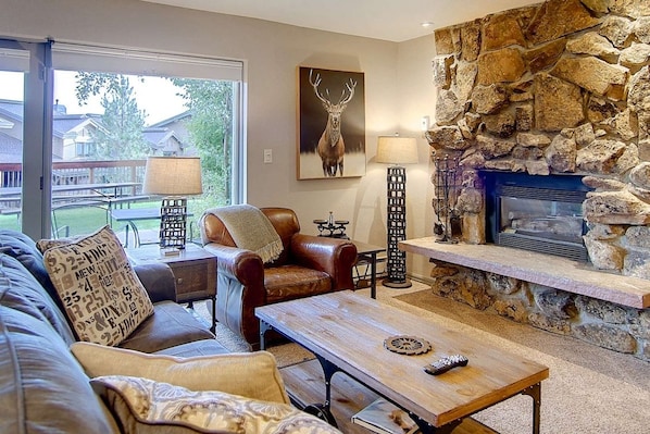 Un salón acogedor con chimenea de piedra, sofá de cuero y vistas al exterior.