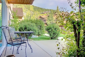 Un patio con mobiliario exterior, vista a una montaña y un edificio con techo inclinado.