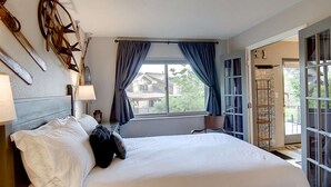 A hotel room with a large bed, a window with curtains, a lamp, and a view of the outside.