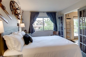 A hotel room with a large bed, a window with curtains, a lamp, and a view of the outside.