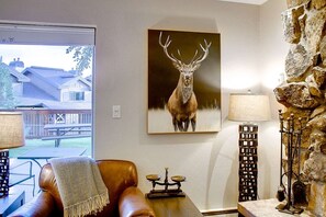 A living room with a leather sofa, a table, a lamp, a stone wall, and a deer painting. - Ski In & Walk Out-Patio with Slope Views-HotTub (Steamboat Springs)