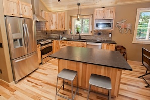 Enjoy cooking in this kitchen with a central island, barstools, stainless steel appliances, and wooden cabinetry.