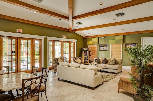 A spacious indoor area with a high ceiling, wooden beams, a large sofa, a dining table with chairs, and a bookshelf.