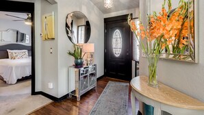 Un couloir moderne avec un miroir rond, une porte noire dotée d’un panneau en verre et un vase rempli de fleurs oranges posé sur une console.