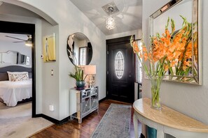 Un ingresso moderno con uno specchio rotondo, una porta nera con un pannello di vetro e un vasetto con fiori arancioni su un tavolo consolle.