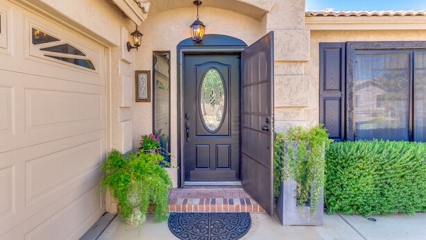 Une maison avec une porte d’entrée noire, un portail de garage et un jardin bien entretenu avec des plantes.