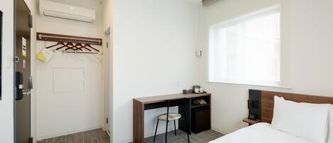 Une chambre d’hôtel comprenant un lit, un bureau, une chaise, une petite table de chevet, une armoire et une fenêtre.