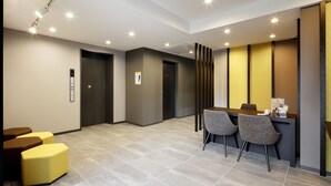 A modern reception area with a reception desk, two grey chairs, and a yellow ottoman. - M’s Hotel Kyoto Station Kizuya (Kyoto)