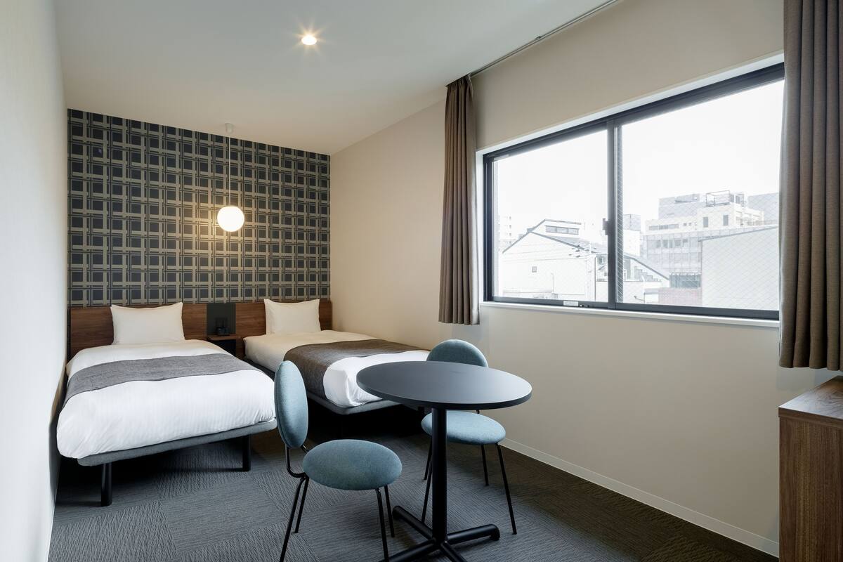 A hotel room with two beds, a round table, and a large window.