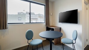 A modern hotel room with a large window, a flat-screen TV mounted on the wall, and two chairs around a small round table. - M’s Hotel Kyoto Station Kizuya (Kyoto)