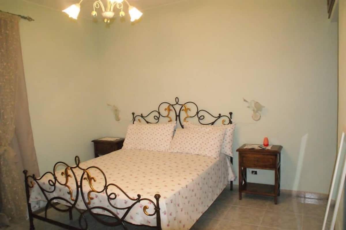 A bedroom with a bed, a nightstand, a wall-mounted shelf, and a chandelier.