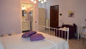 Ein Schlafzimmer mit Bett, Schminktisch, Spiegel, Tür und einem kleinen Tisch mit Stuhl.