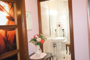 A bathroom with a sink, mirror, and a vase with flowers on a small table.