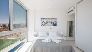 A modern hotel room with a large bed, a painting on the wall, and a view of the city through the window.
