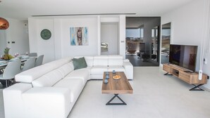 A modern living room with a white sectional sofa, a wooden coffee table, and a flat-screen TV on a wooden stand.