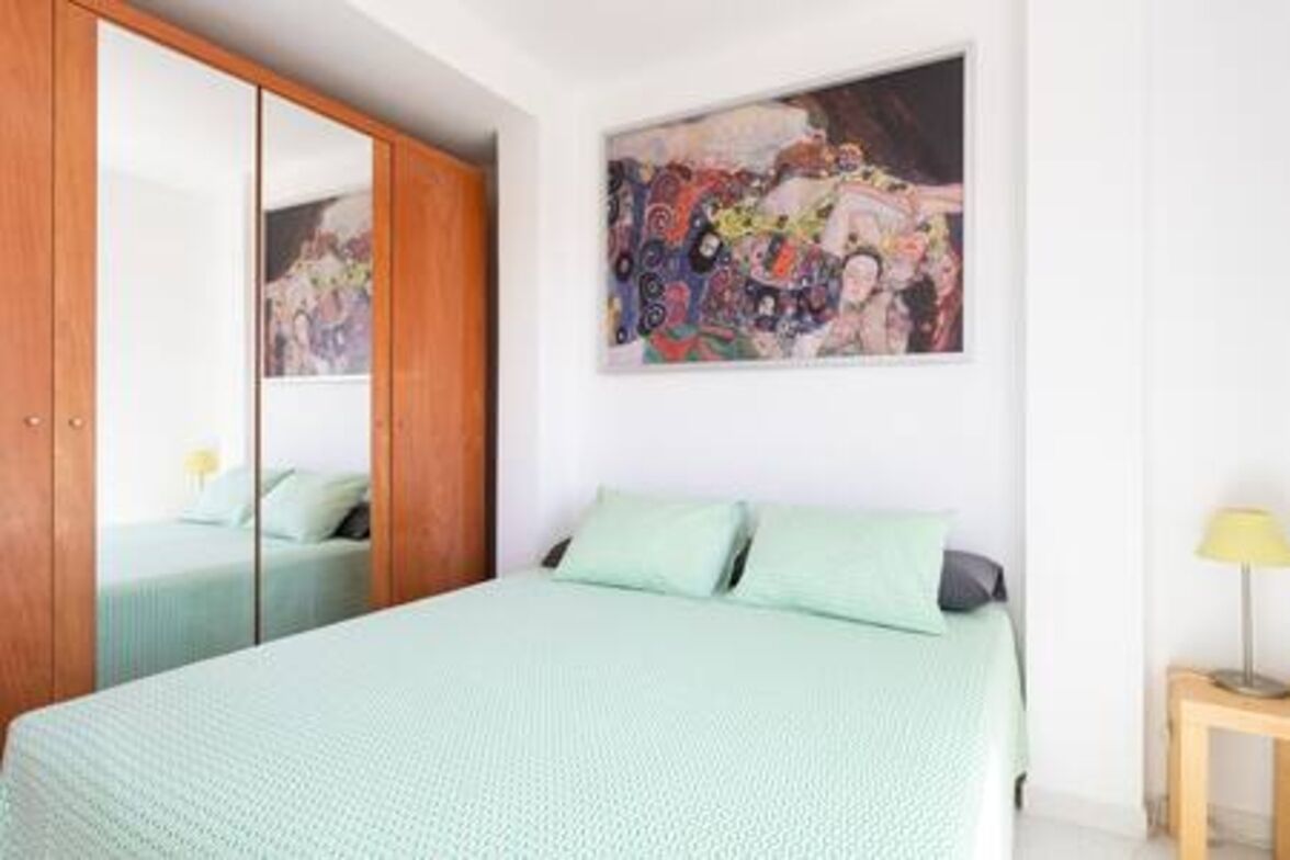 Un dormitorio con cama, un armario, un cuadro en la pared y una mesita de noche con lámpara.